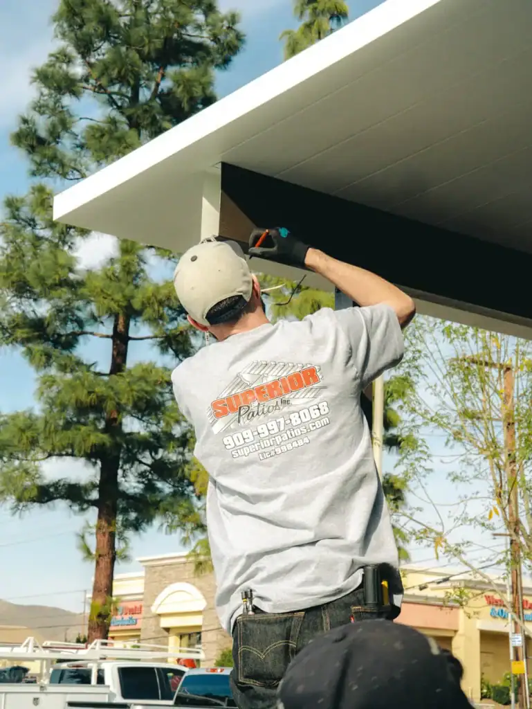 A Superior Patios technician installing an aluminum patio cover under clear skies