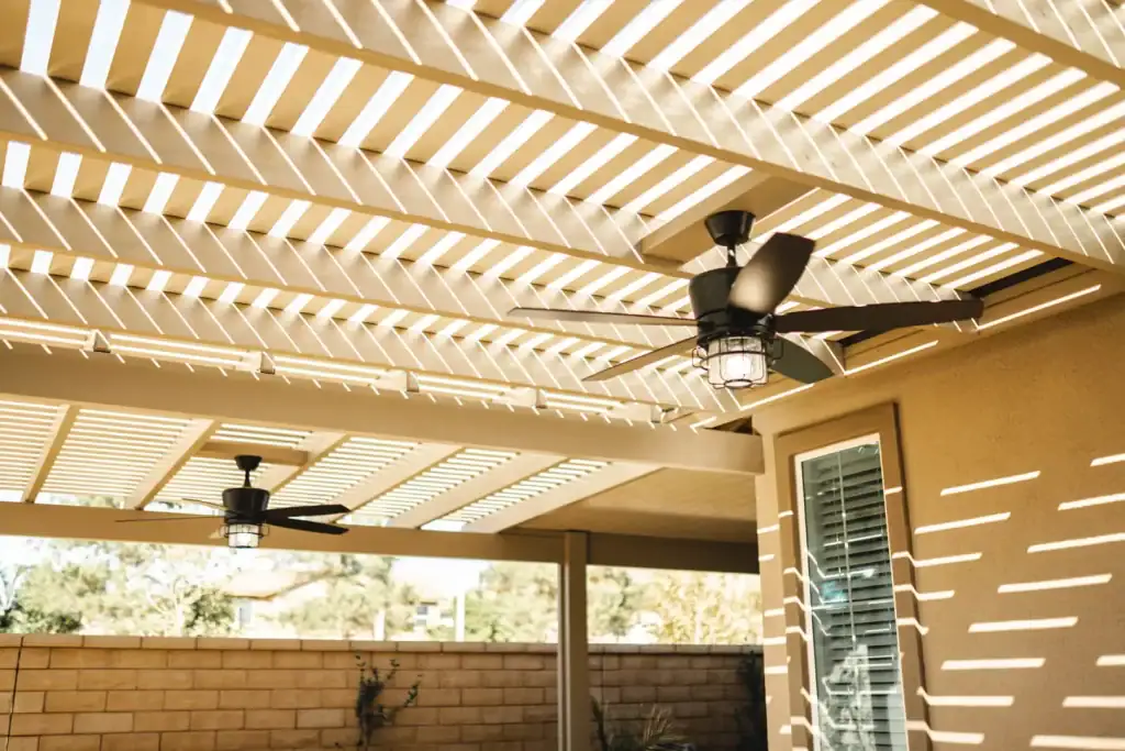 Aluminum pergola patio cover casting striped shadows, featuring modern ceiling fans