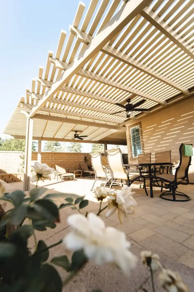 White lattice patio cover casting striped shadows over a cozy patio with chairs and ceiling fans